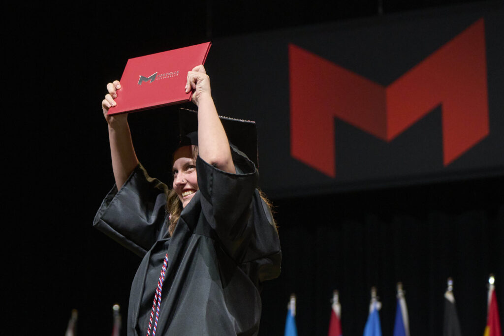 Woman holding up her diploma and smailing.